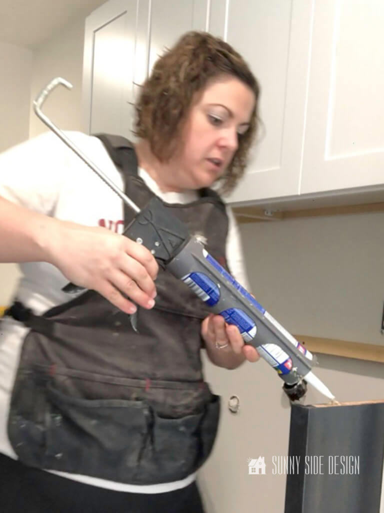 Woman with caulk gun applying constructional adhesive to top of the base for the laundry room folding table.