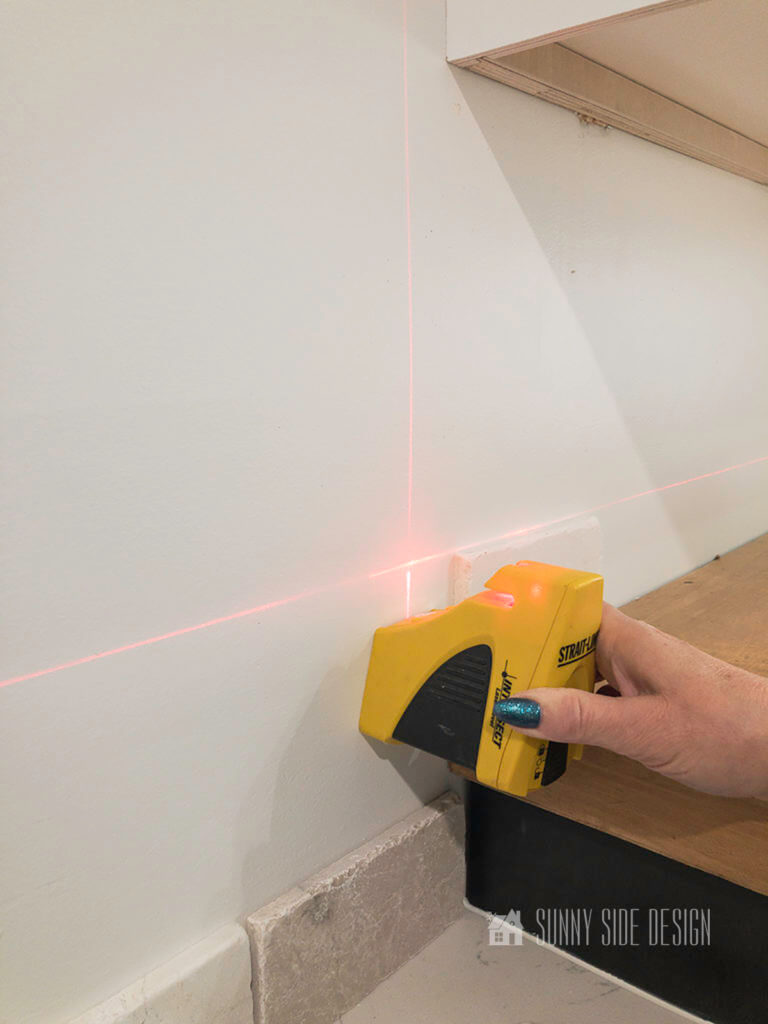 Woman's hand holding a laser level along the top of a row of marble tiles.