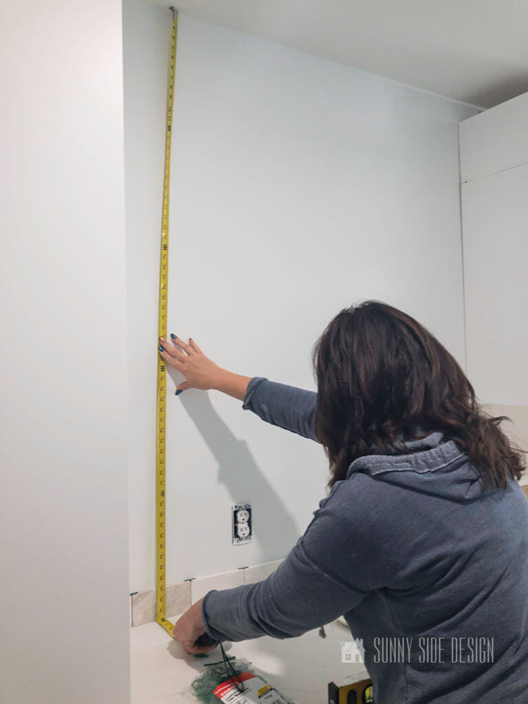 Woman holding a measuring tape on the wall. Determining the height of the tiles before install the backsplash.