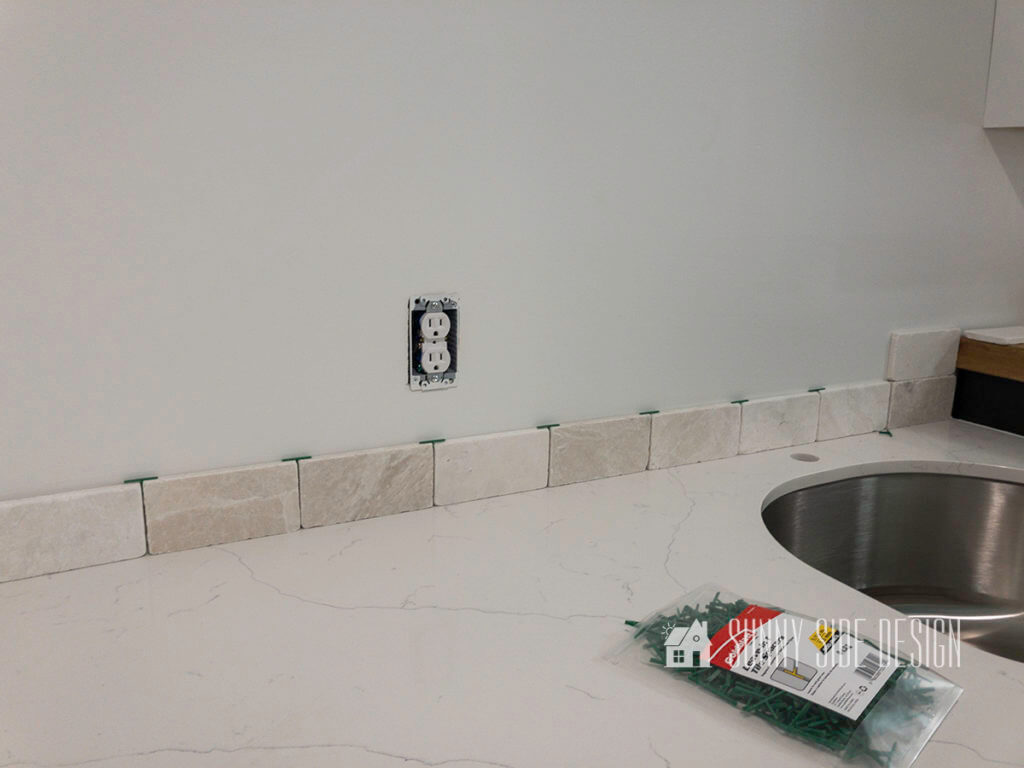Placing tiles and spacers along wall to determine pattern and placement before install a tile backsplash.