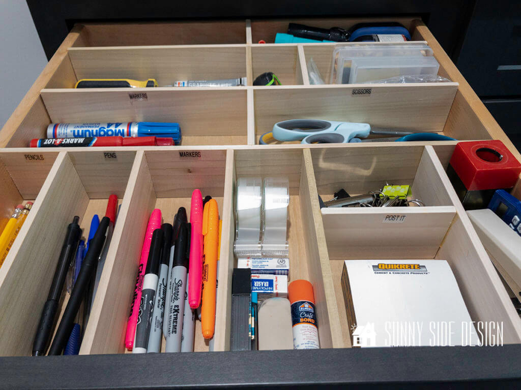 Tame the clutter of a junk drawer with this DIY custom wood organizer. Each section is labeled and filled with household items like pencils, pens, markers, tape, glue, erasers, note paper, stapler, clips, tools, scissors, rubber bands and flashlights.