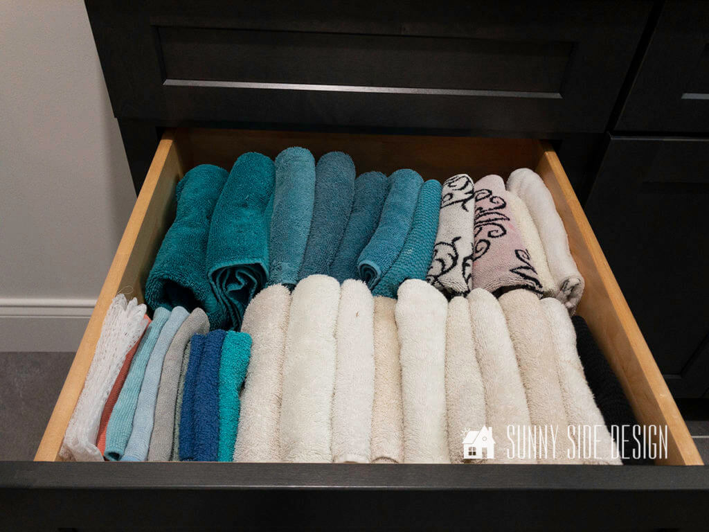 Open drawer filled with cleaning rags and towels placed vertically in the drawer for better organization.