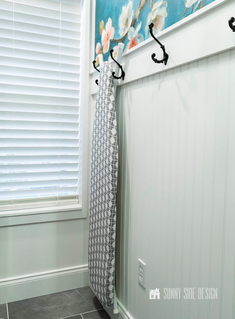 Hanging storage with hooks on bead board wall for ironing board.
