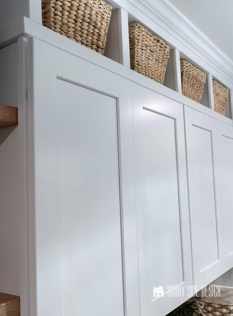 Laundry room organization ideas, white shaker cabinets are placed abover the laundry room appliances. Above the cabinets cubbies were added for basket storage, topped with crown molding.