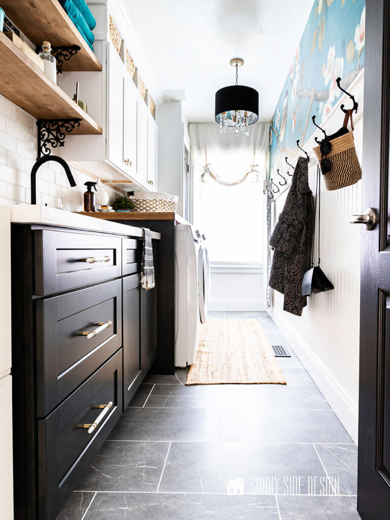 The Laundry room reveal. Grey marble floor, bead board and wallpaper mudroom wall, modern glam chandelier, charcoal stained shaker lower cabinets, white shaker upper cabinets, marble and champagne gold pulls and knobs, natural wood open shelving with black iron brackets.