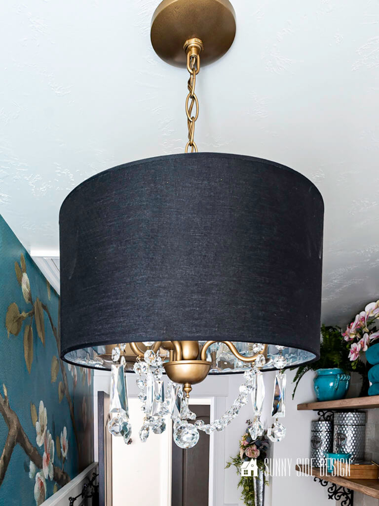 Modern glam chandelier in laundry room, with a black shade, gold, metal fixture with vintage crystals.