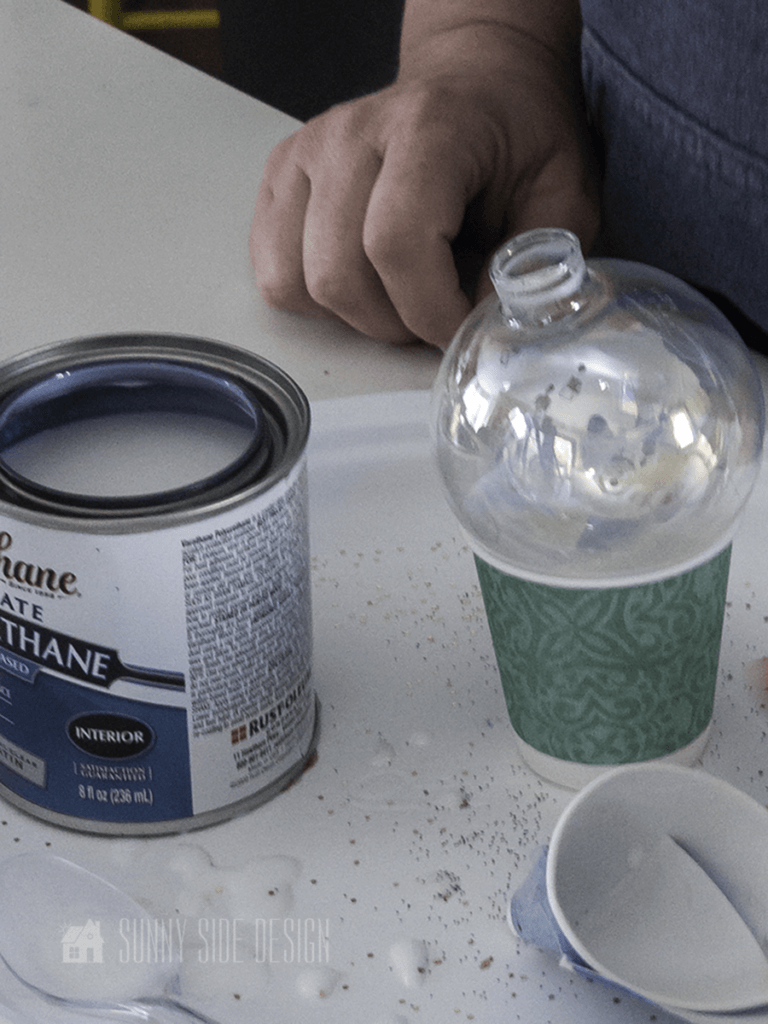 Clear glass ornament setting on a paper cup and a can of polyurethane.