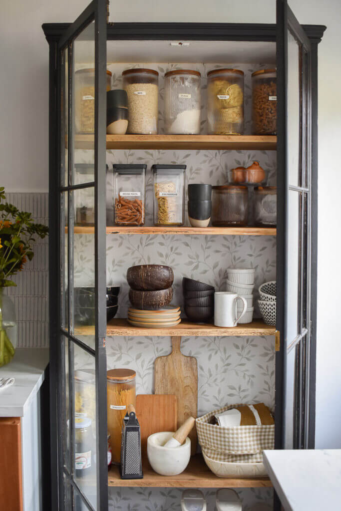 Pantry Organization Ideas - Vintage cabinet is refinished with paint and wallpaper. Clear containers organize dry goods along with bowls, mugs, and cutting boards.