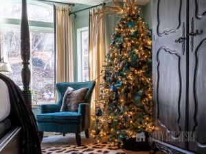 How to decorate Master bedroom for Christmas with slate blue walls, cheetah print rug, black armoire, peacock blue modern wing back chair and a flocked christmas tree with blue ribbon, gold glitter balls, black glitter ornaments and glitter gold leaf picks.