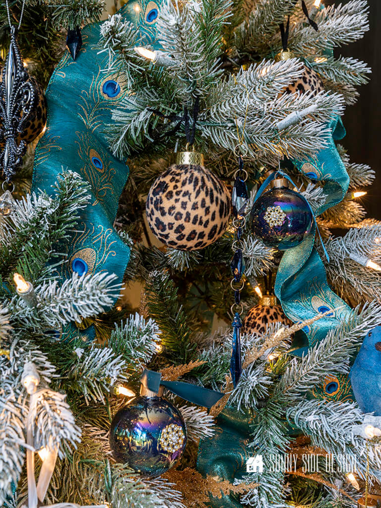 Decorate bedroom for Christmas. Flocked Christmas tree with cheetah ball ornaments, gold glitter ball ornaments, blue jewels, blue birds, black glitter ball ornaments, gold leaf picks and peacock blue ribbon.
