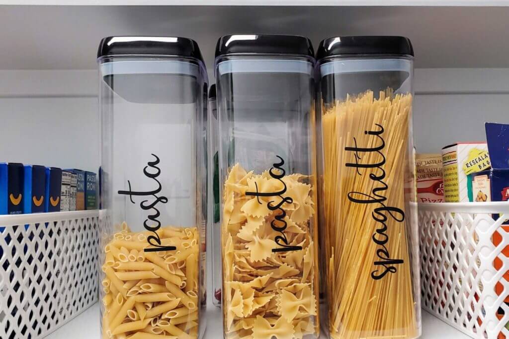 Clear plastic containers store pasta, labeled with black vinyl lettering.