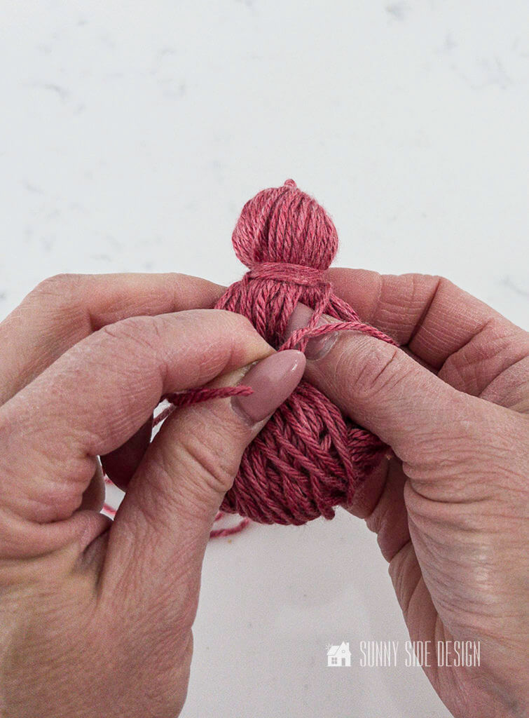 Woman's hands wrapping length of yarn around top of tassel for the Valentine pillow cover.