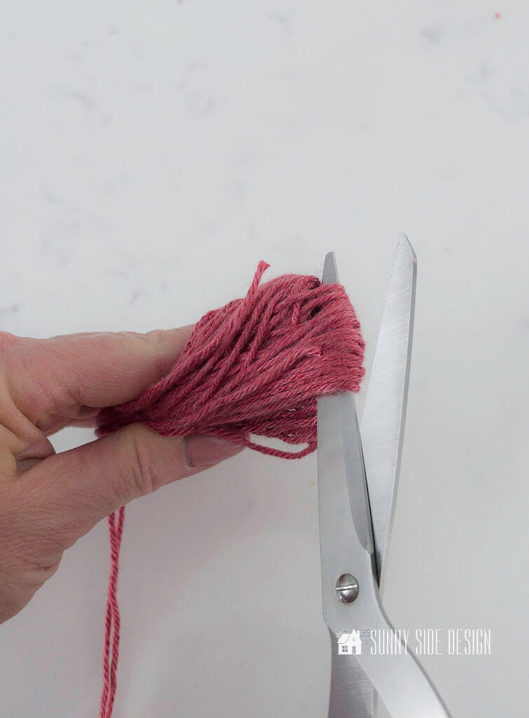 Woman's hand cutting the lower looped edge of the yarn to form a tassel for the no sew Valentine pillow cover.