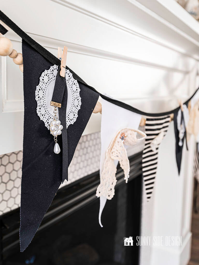 Black and white fabric bunting hanging on mantle with vintage lace, brooches and bookmarks creating a neutral Valentine garland.