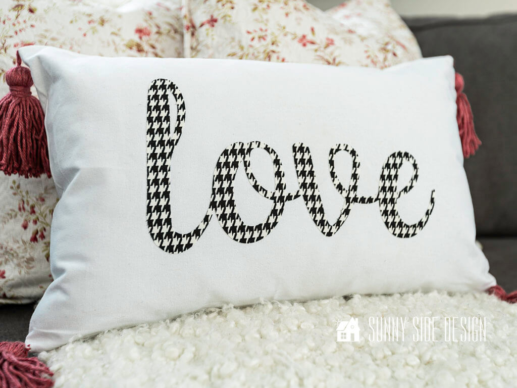 Valentine Pillow cover with black and white houndstooth "love" and dusty rose tassels, sitting on sofa with floral pillows.