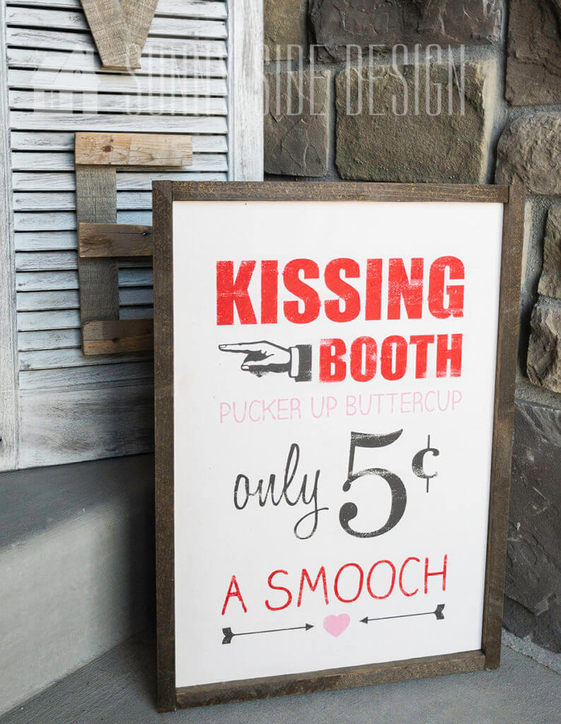 Hand painted wooden art, red letters speilling "kissing booth", pink letters: "pucker up buttercup", script "only" $.05, red lettering "a smooch" with a wooden frame.