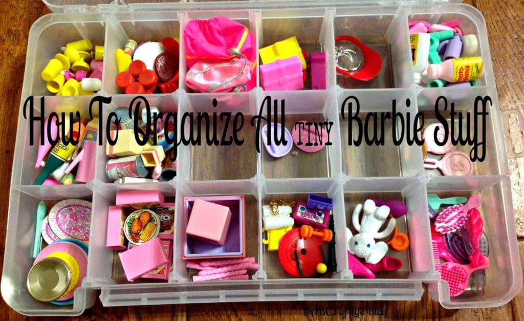 Small Barbie doll accessories are organized in a craft supply container.