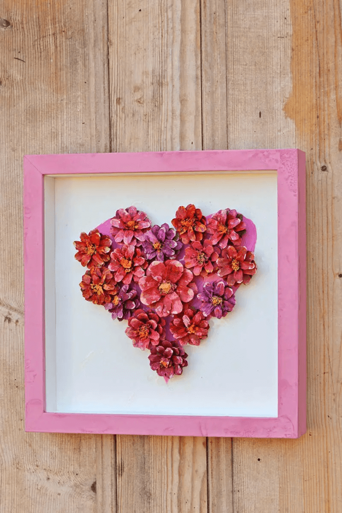 DIY Valentine's Day decorations, heart formed with pine cone flowers painted pink, red and purple mounted in a pink frame.