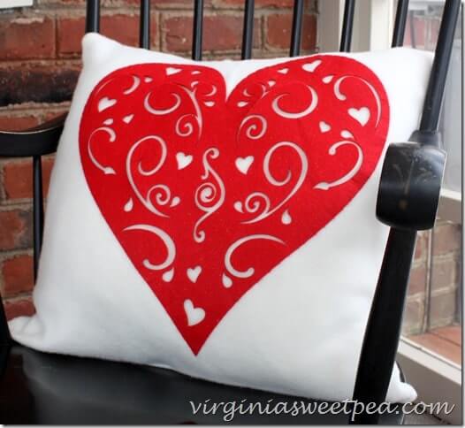 White pillow with a red heart cutout on a black spindle chair.