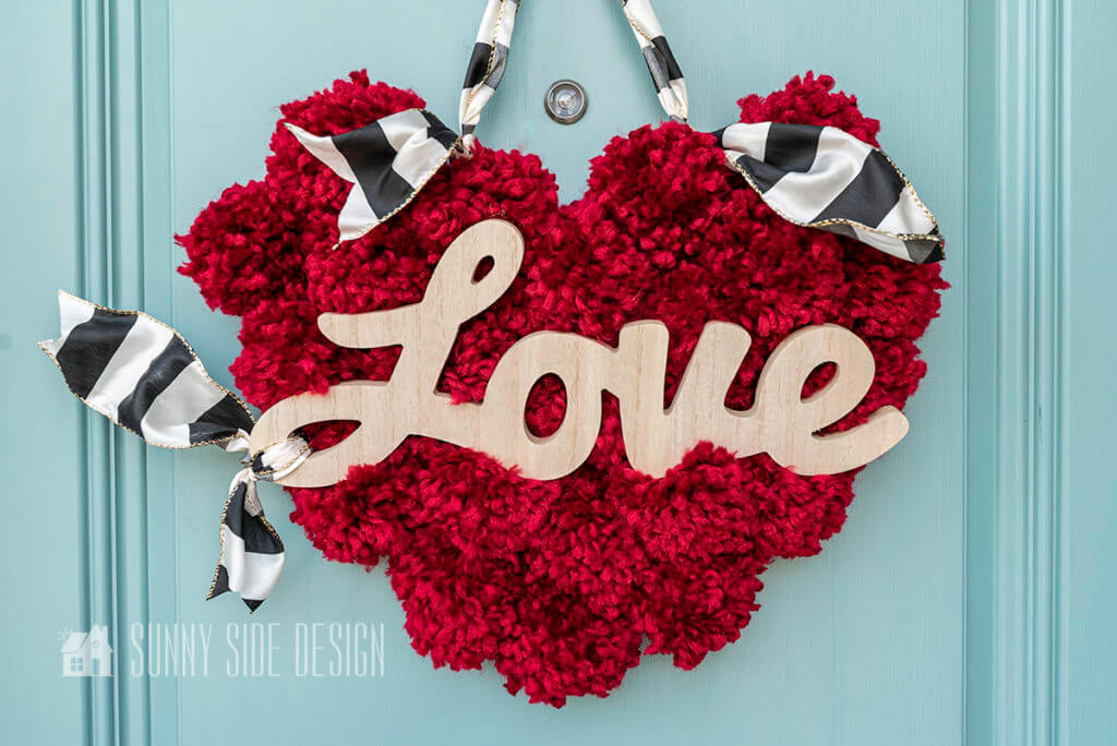 DIY Valentine's Day decorations, red pom pom wreath, with wooden script "love" and black and white ribbon.