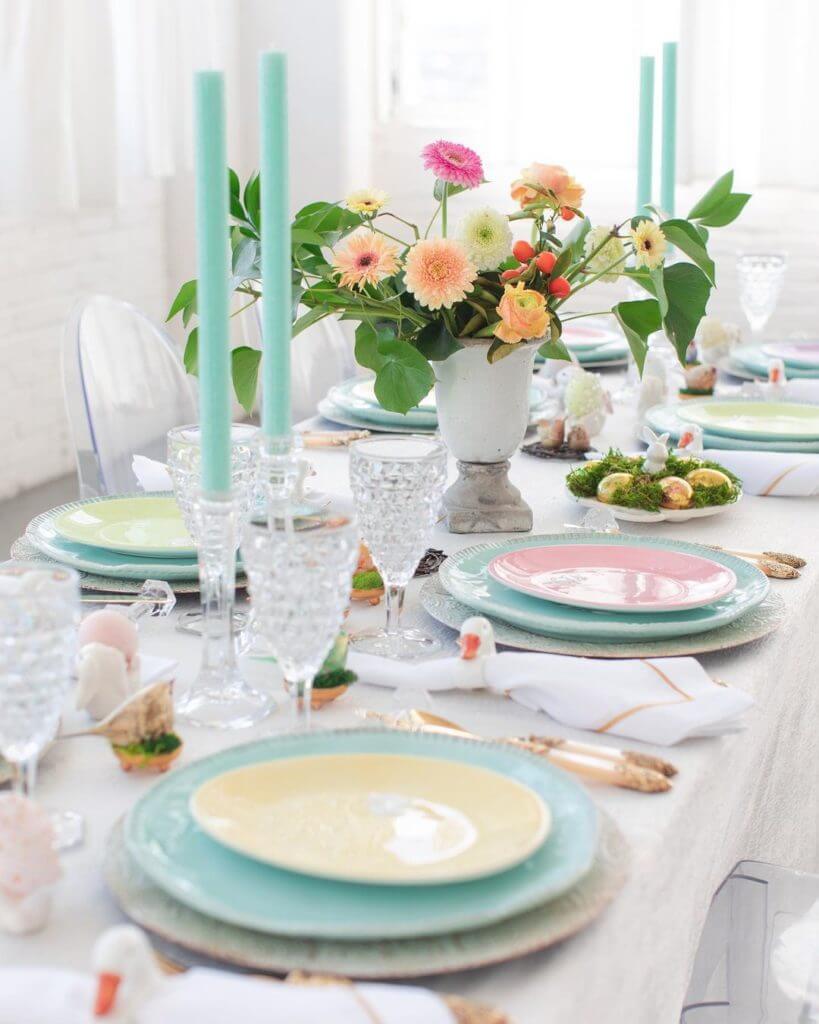 Easter Tablescape ideas, pastel plates layered over a white tablebcloth. White napkin with a duck napkin ring, crystal stemware. Light blue candles with bouquest of zinnias in a white vase.