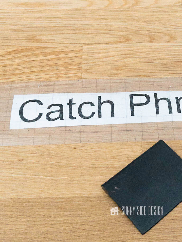 Cut vinyl letters, spell out "Catch Phrase" game. Placed on a wooden table top with a black rubbing tool.