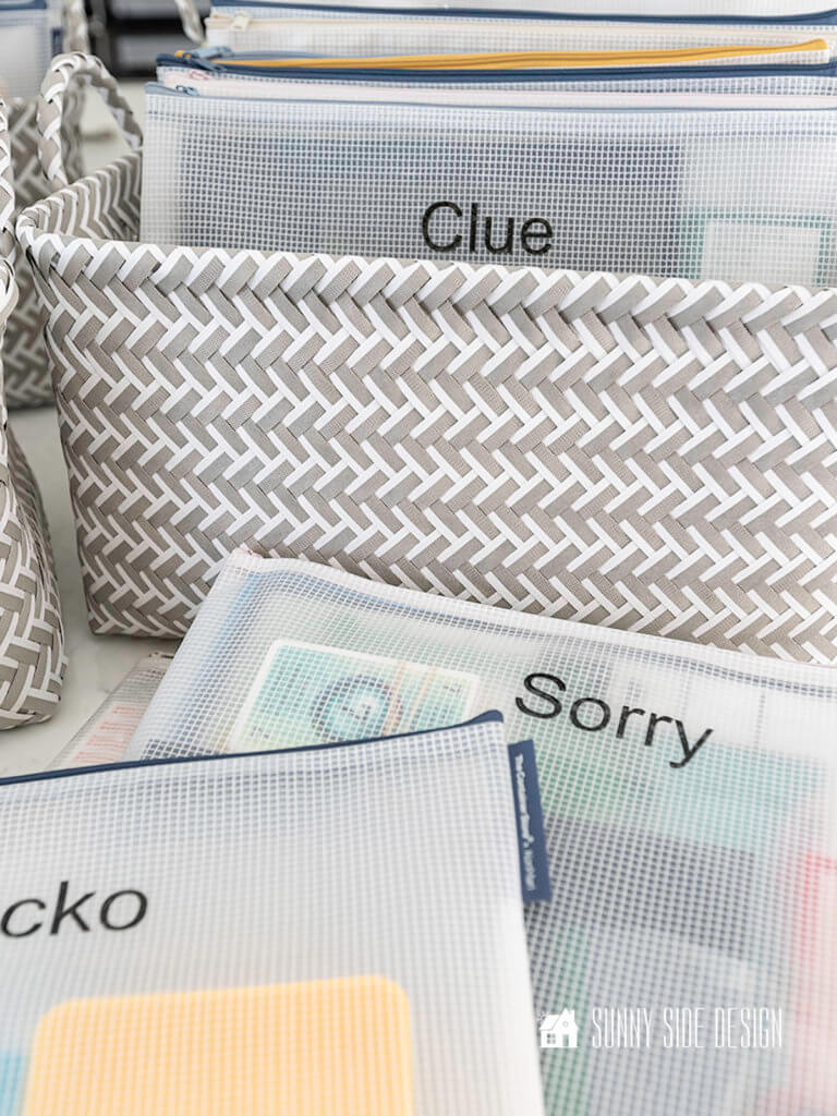 Organizing games, family board games of Racko, Sorry and Clue are place in zippered vinyl pouches and stored in a white an gray basket