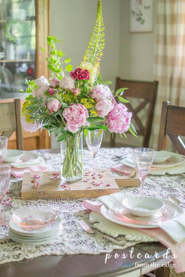 Lace tablecloth with white and pink depression glass plates. Simple centerpiece with pink peonies, yellow yarrow and greenery.