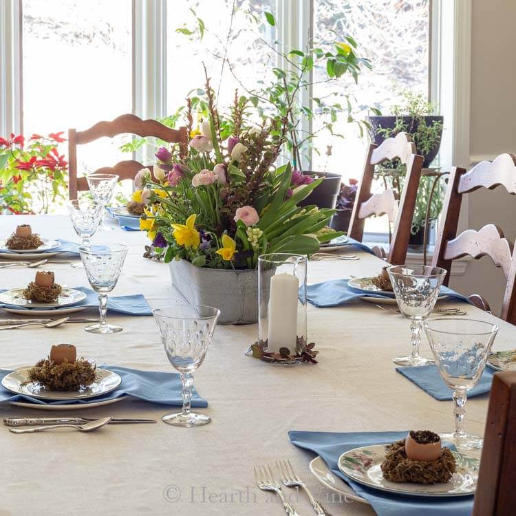 Easter Tablescape ideas. Linen tablecloth with floral plates, blue napkins. Centerpiece is fresh spring flowers in a galvanized trough.