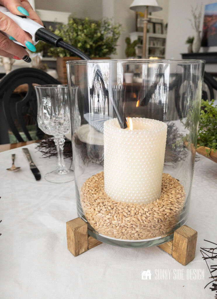 Woman's hand holding a lighter lighting candle in glass hurrican on the Easter table.