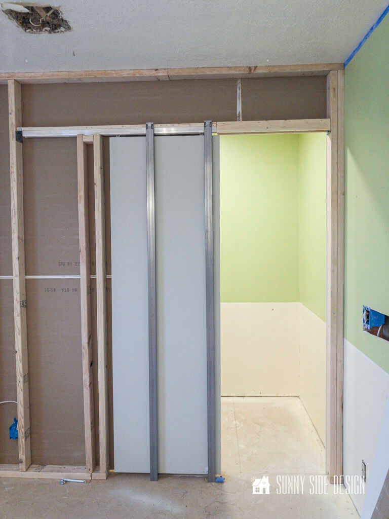 Framed walk-in closet area with hardware for pocket door. Before apple green wall color.
