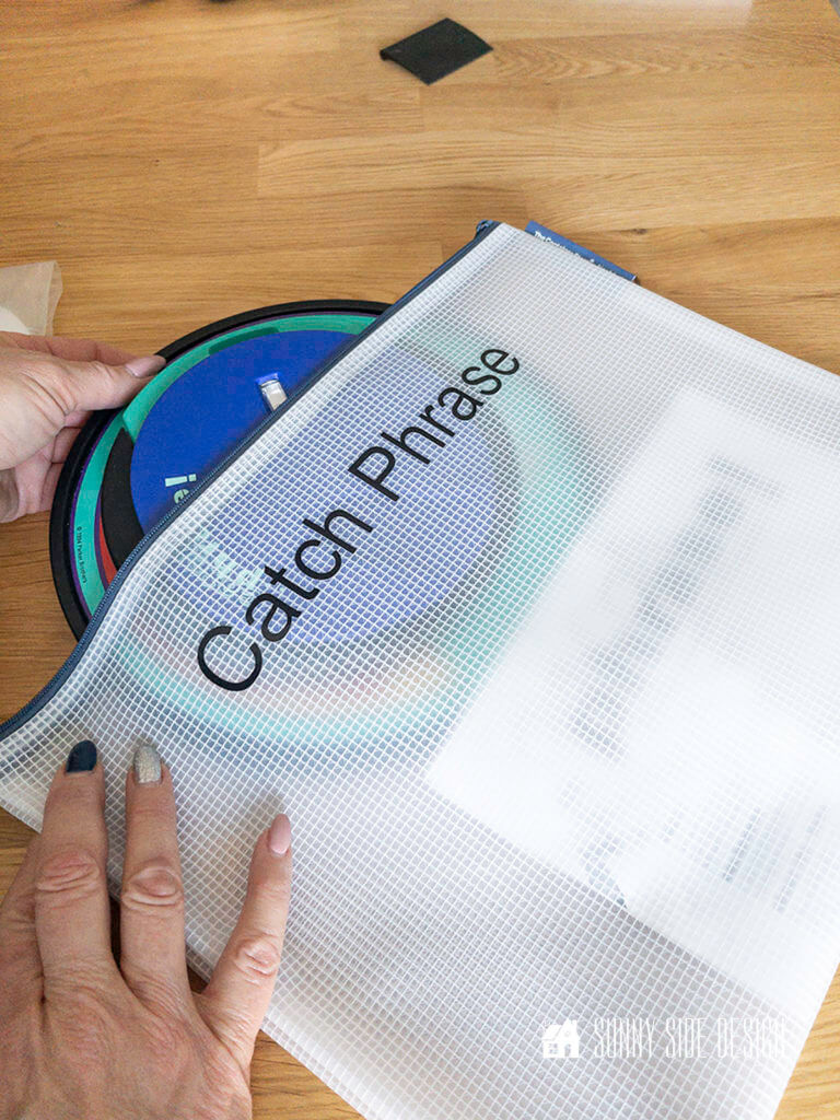 Woman's hands placing "catch phrase" game parts into the zippered vinyl pouch.