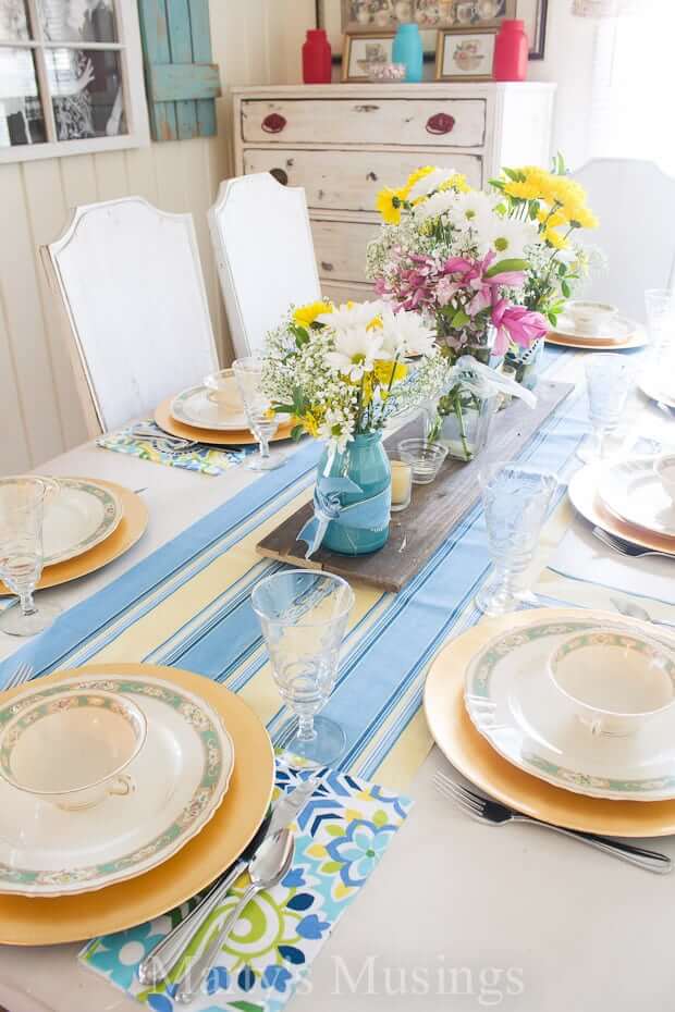 Easter Tablescape ideas, blue and yellow tablerunner, with fresh flowers in glass vases. Blue and green floral placemats, vntage china and stemware.