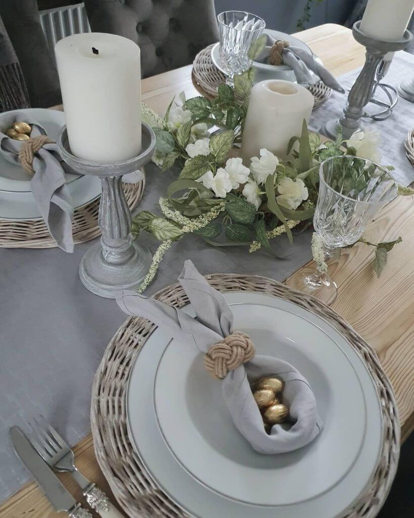 Grey tablerunner, with white washed rattan chargers, white china dishes with a grey napkin foled into bunny ears with eggs n center. White candle centerpiece.