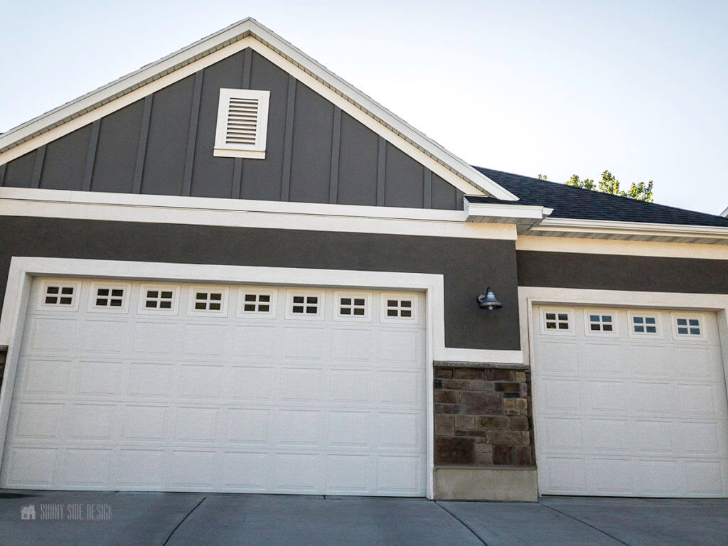 Curb appeal ideas, home facade with dark grey stucco and a grey, taupe stone with white trim and  white garage doors.