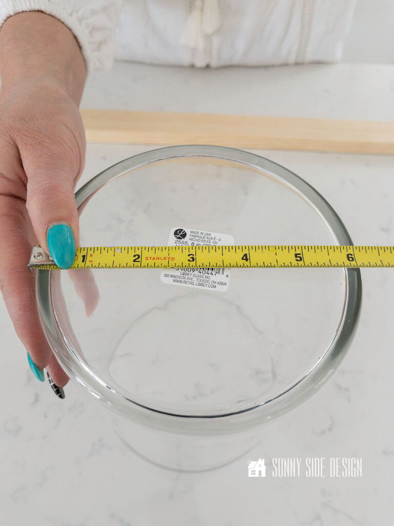Woman's holding a tape measure across the diameter of the glass hurricane.