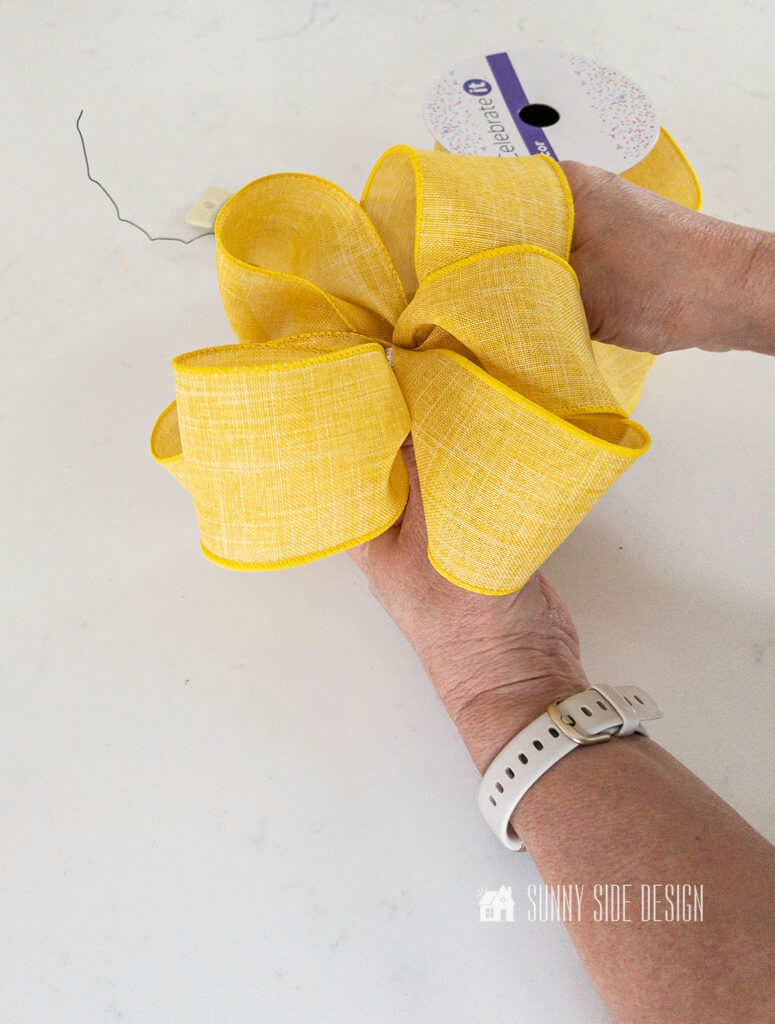 Woman's hand forming a looped bow with yellow ribbon.