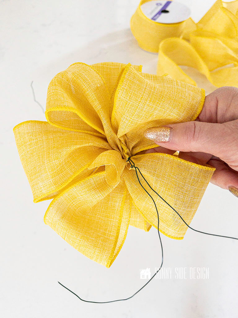 Woman's hand holding the finished yellow looped bow for the summer garden wreath.