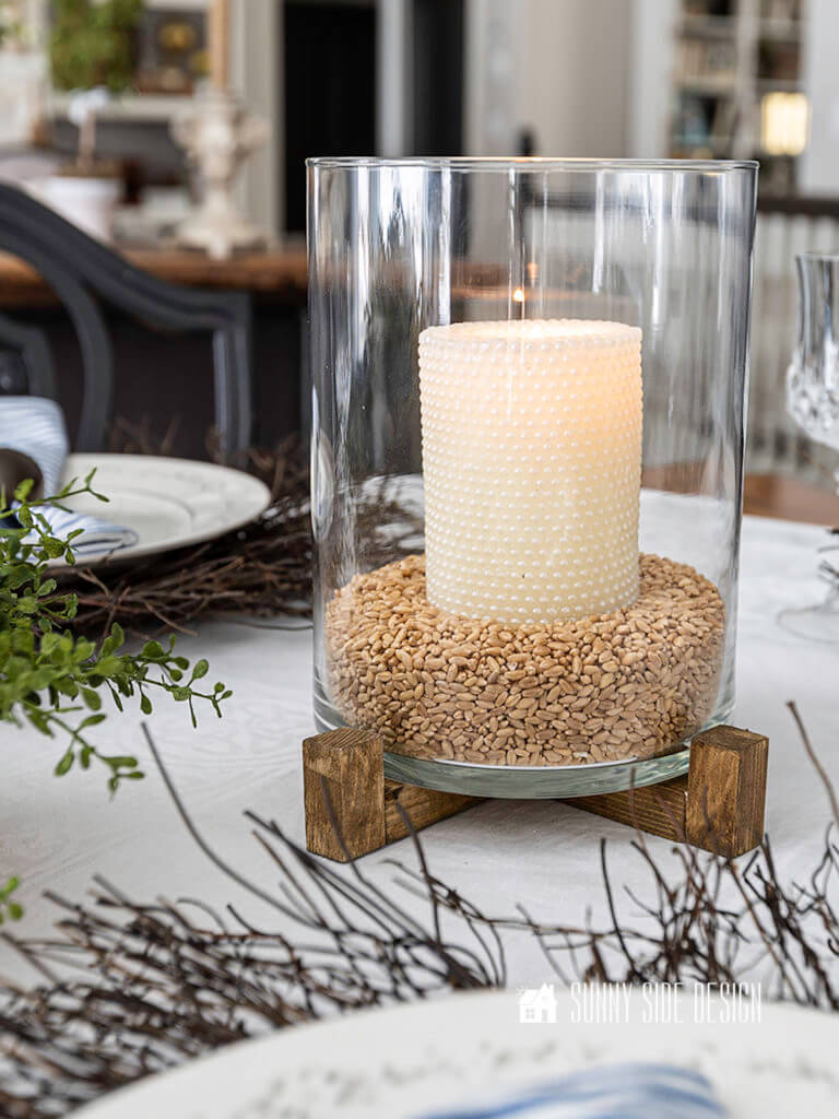 Pottery Barn dupe, lit candle in a glass hurricane on a wood stand.