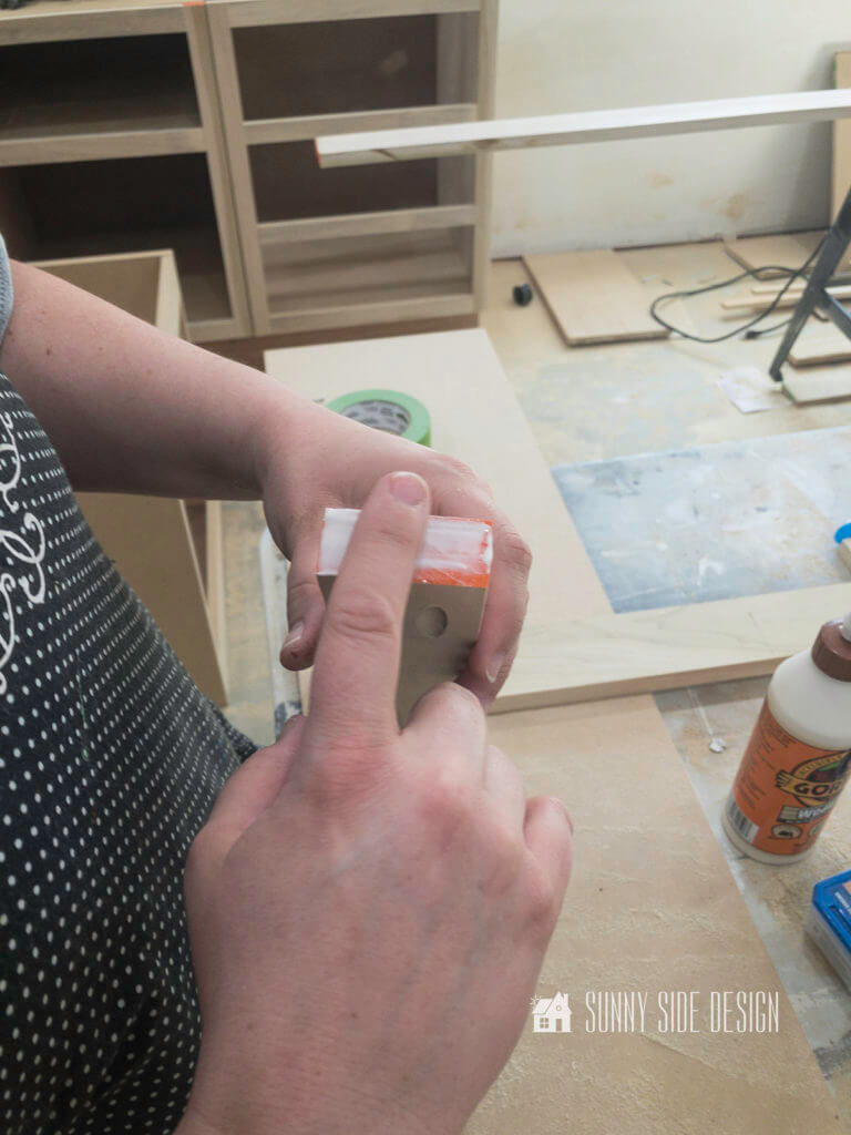 Woman spreads wood glue on the end of a board for the face frame for the cabinet.