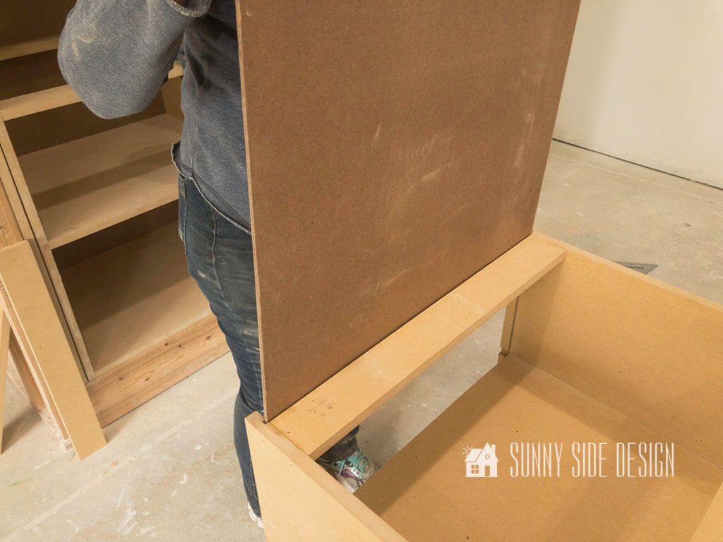 Woman slides in a piece of hardboard tempered panel into the back groove while make a cabinet.