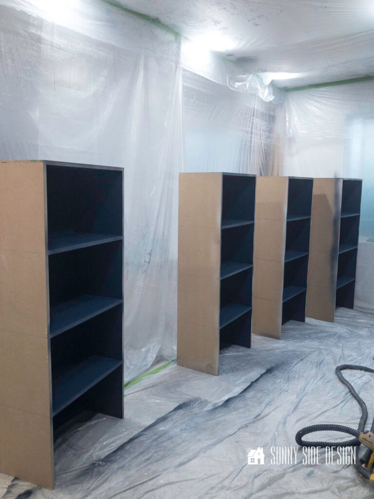 4 book shelves painted navy blue sitting on a plastic paint tarp.