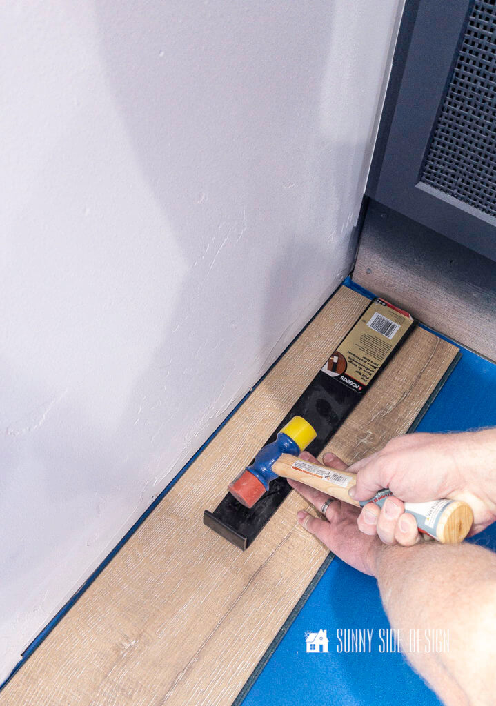 Man's hand holding pull bar at end of row, tapping with a rubber mallet when installing a laminate floor over concrete.