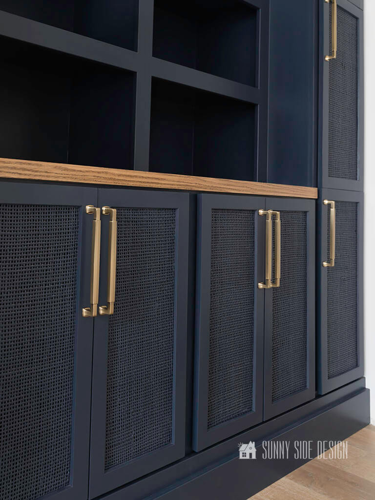 Built in entertainment center with Hale Navy blue painted cabinets and shelves with rattan doors and champagne gold hardware.