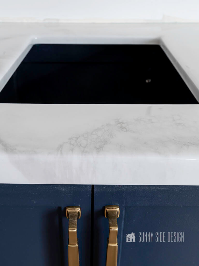 DIY epoxy countertop with a carrara marble look and navy blue cabinets with champagne gold hardware.