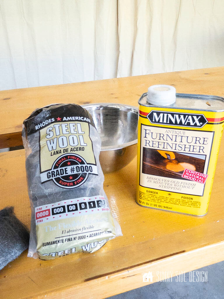Steel wool, stainless steel bowl and Minwax antique furiture refinisher setting on large plank of wood.