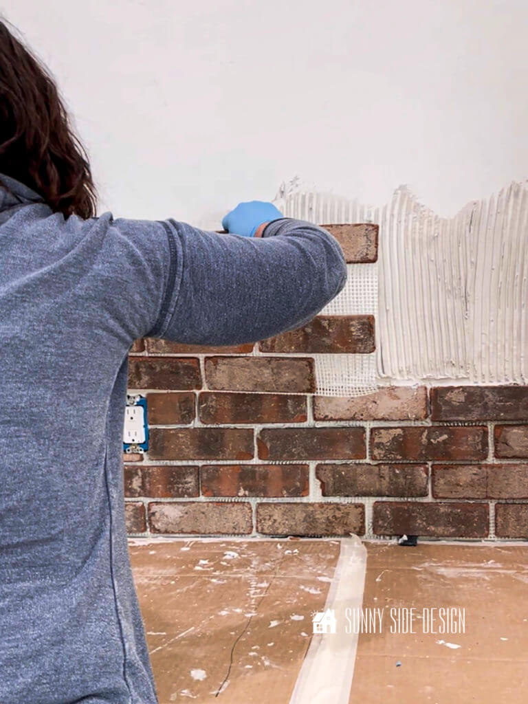 Woman holding a mesh sheet of the brick veneer to apply to the mortar on the wall.