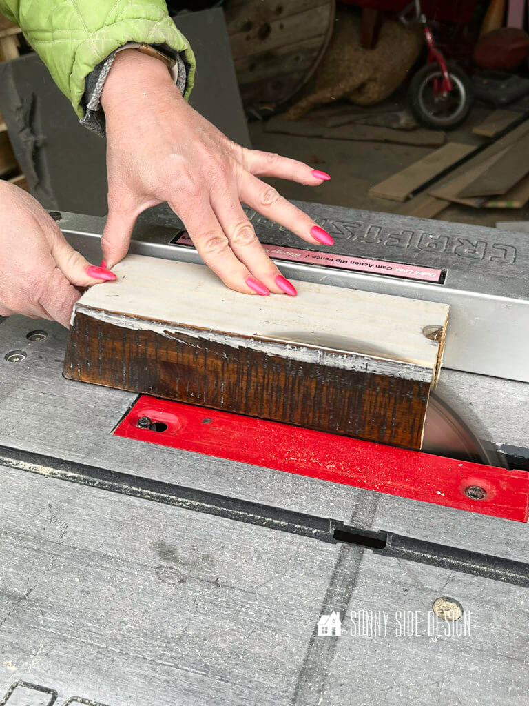 Woman's hand pushing a piece of wood through the table saw.
