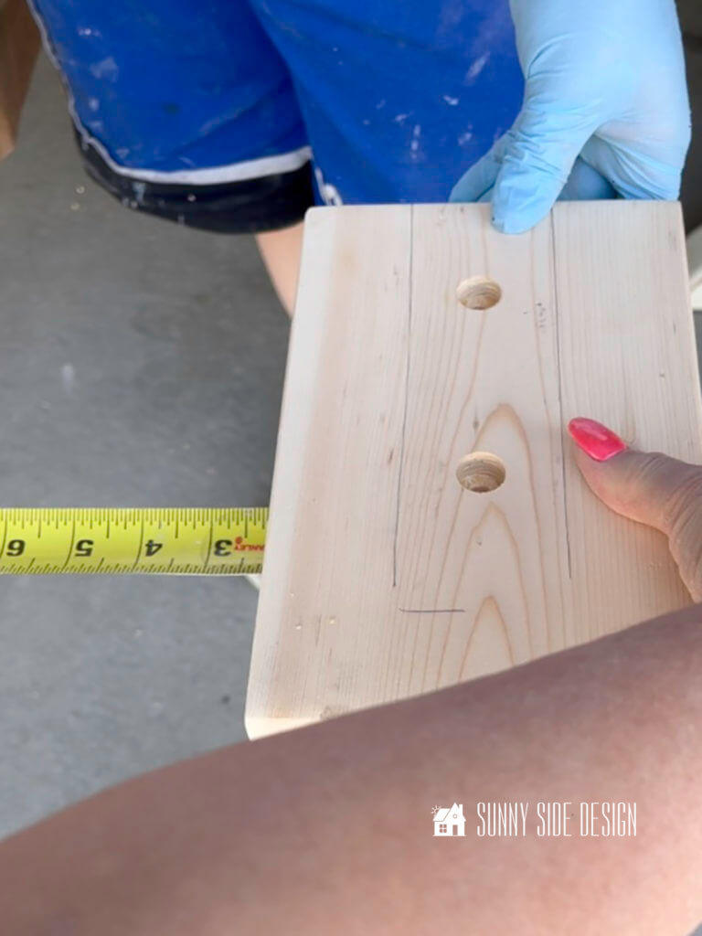 A piece of pine wood with 2 countersink drilled holes is being centered over the sofa table leg.