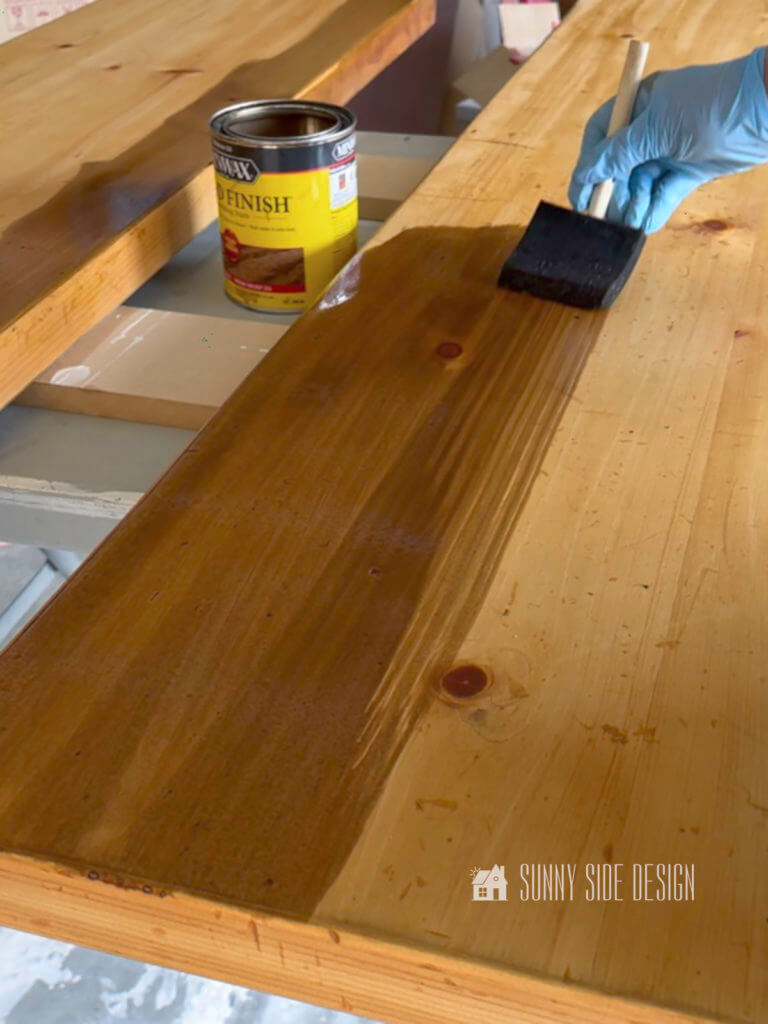 Woman's gloved hand applying stain to wood for the DIY sofa table.